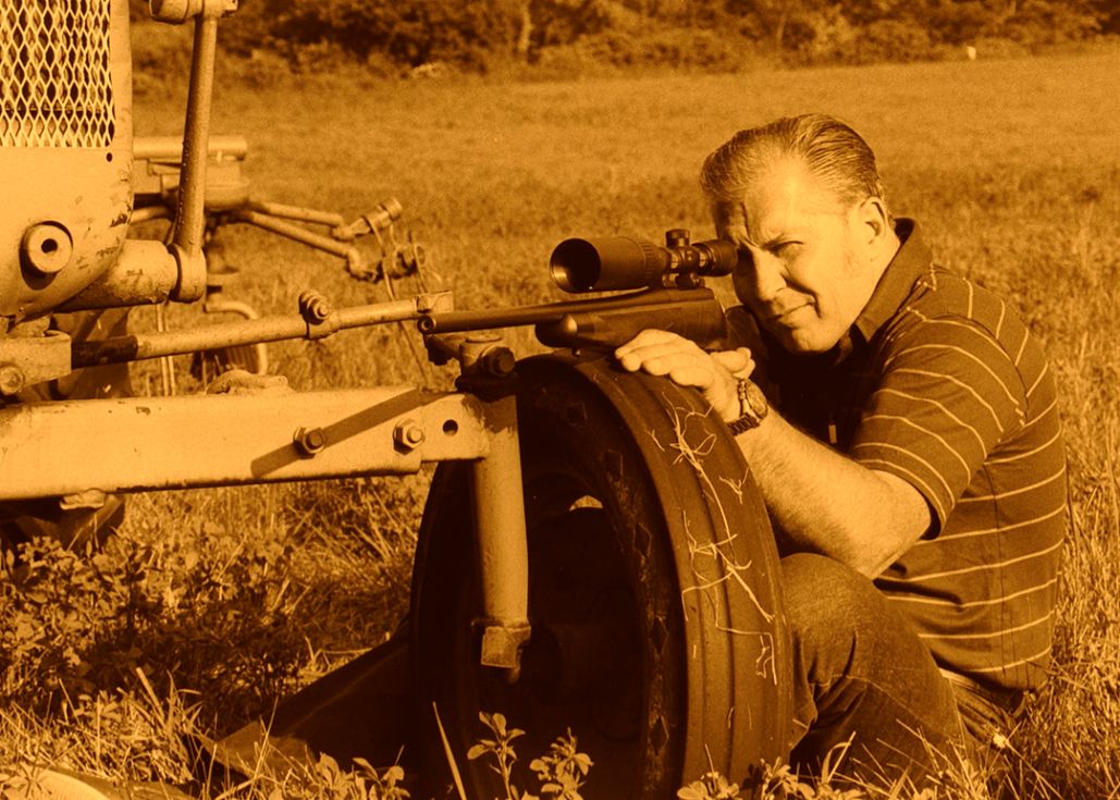 Stan is shown in the field with his rifle. The photo has been tinted to give it the look of a black and white print.
